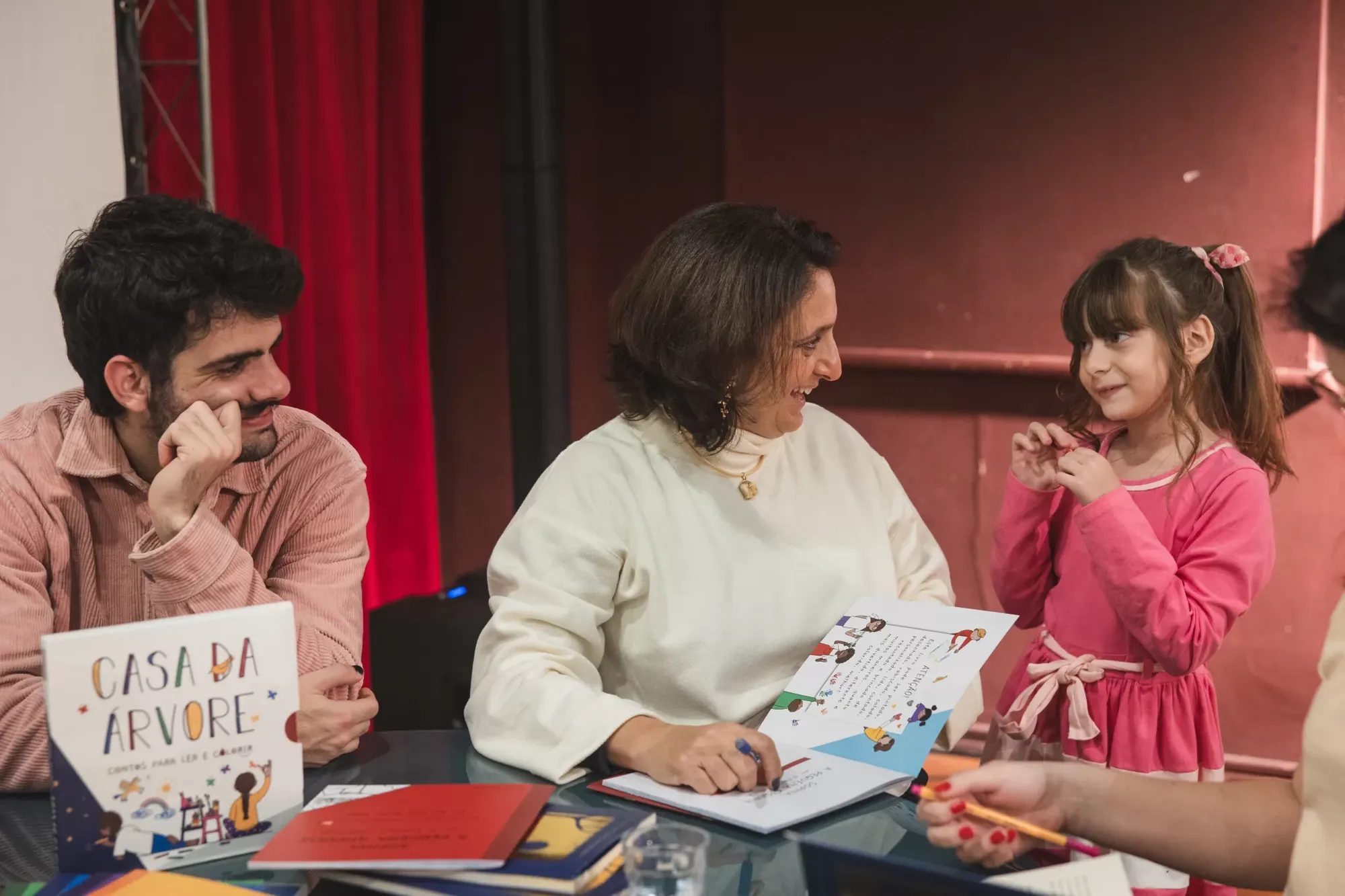 Mesa com livros e uma leitora criança conversando com os autores